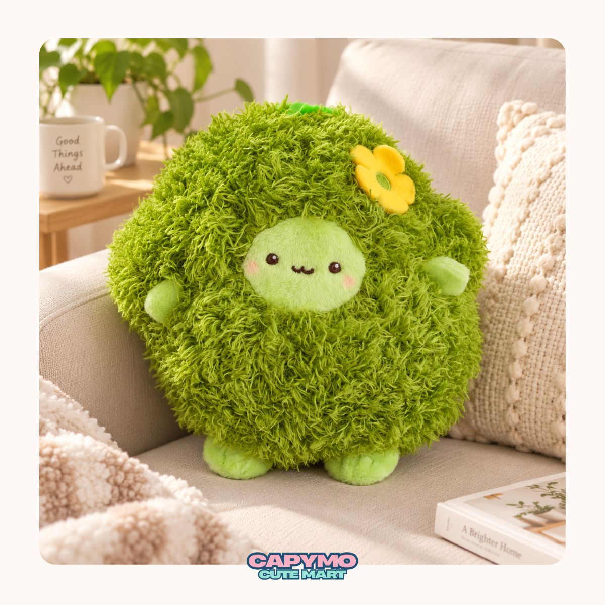 A cute green plush avocado keychain with a smiling face and leafy top, hanging from a beige canvas tote bag on a wooden table with a blurred book and plant in the background.