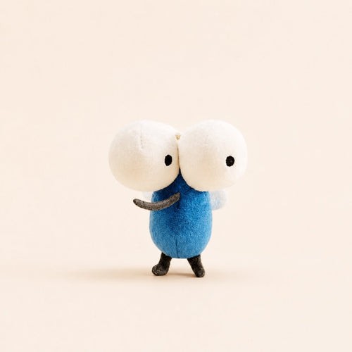 A small plush toy figure with two large white round heads, black eyes, a blue body, and small dark legs, standing against a plain warm beige background.