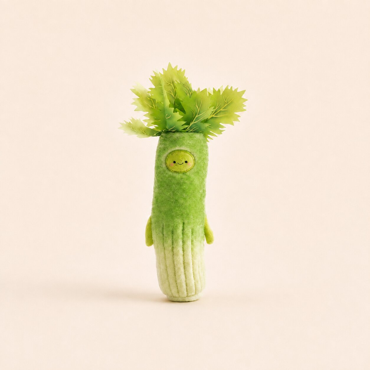 A cute, small plush vegetable character designed like a leek or celery, made from light green and white felt fabric with a small embroidered yellow smiley face and green leafy top, standing against a solid pale beige background.