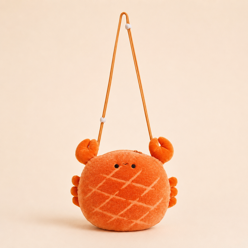 An orange plush crab shoulder bag with a textured pattern, small embroidered eyes, and a thin orange strap, set against a solid beige background.