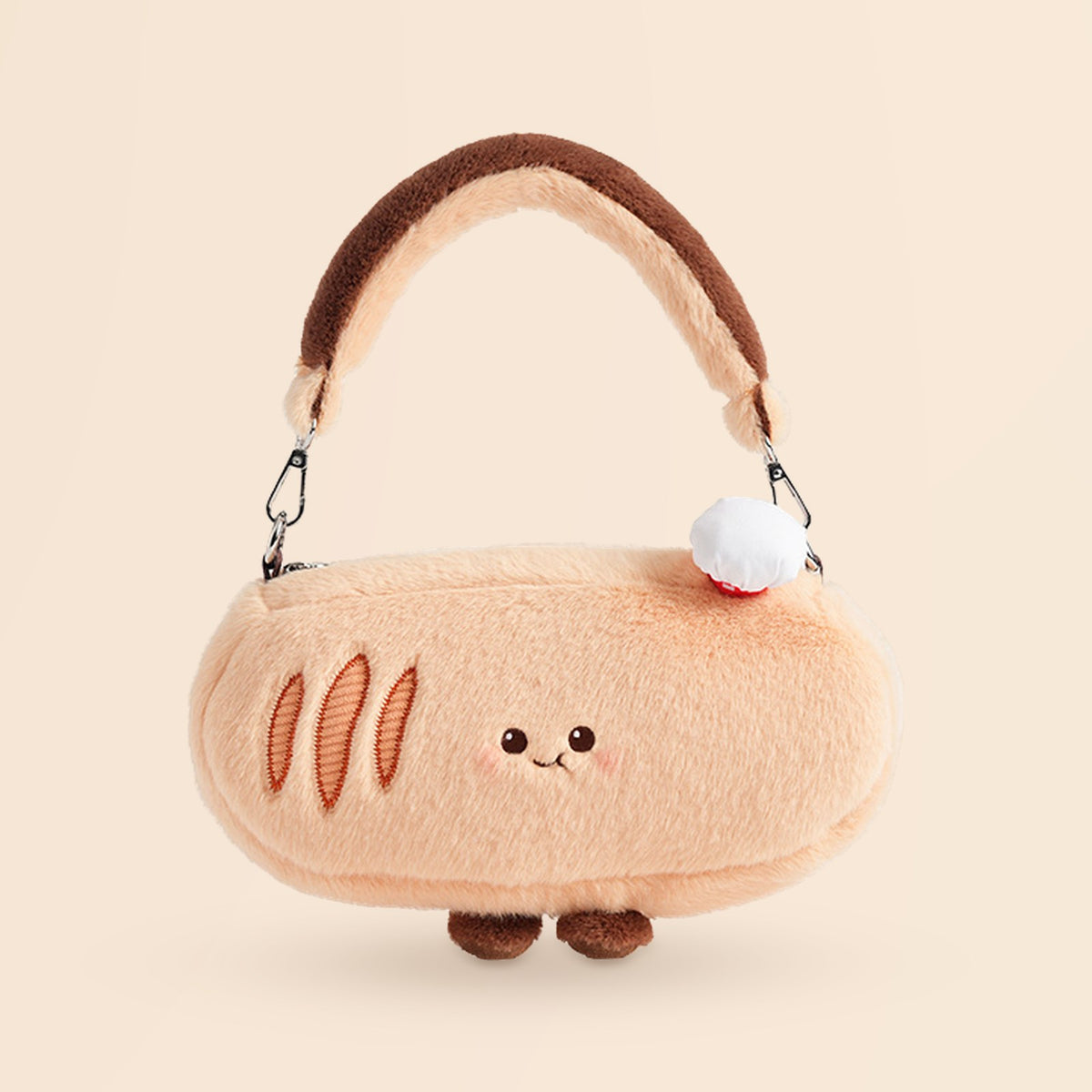 A plush bread-shaped handbag in a soft peach-beige color with embroidered crust details, a brown handle, small brown feet, and a white pom-pom accent, shown on a plain warm beige background.