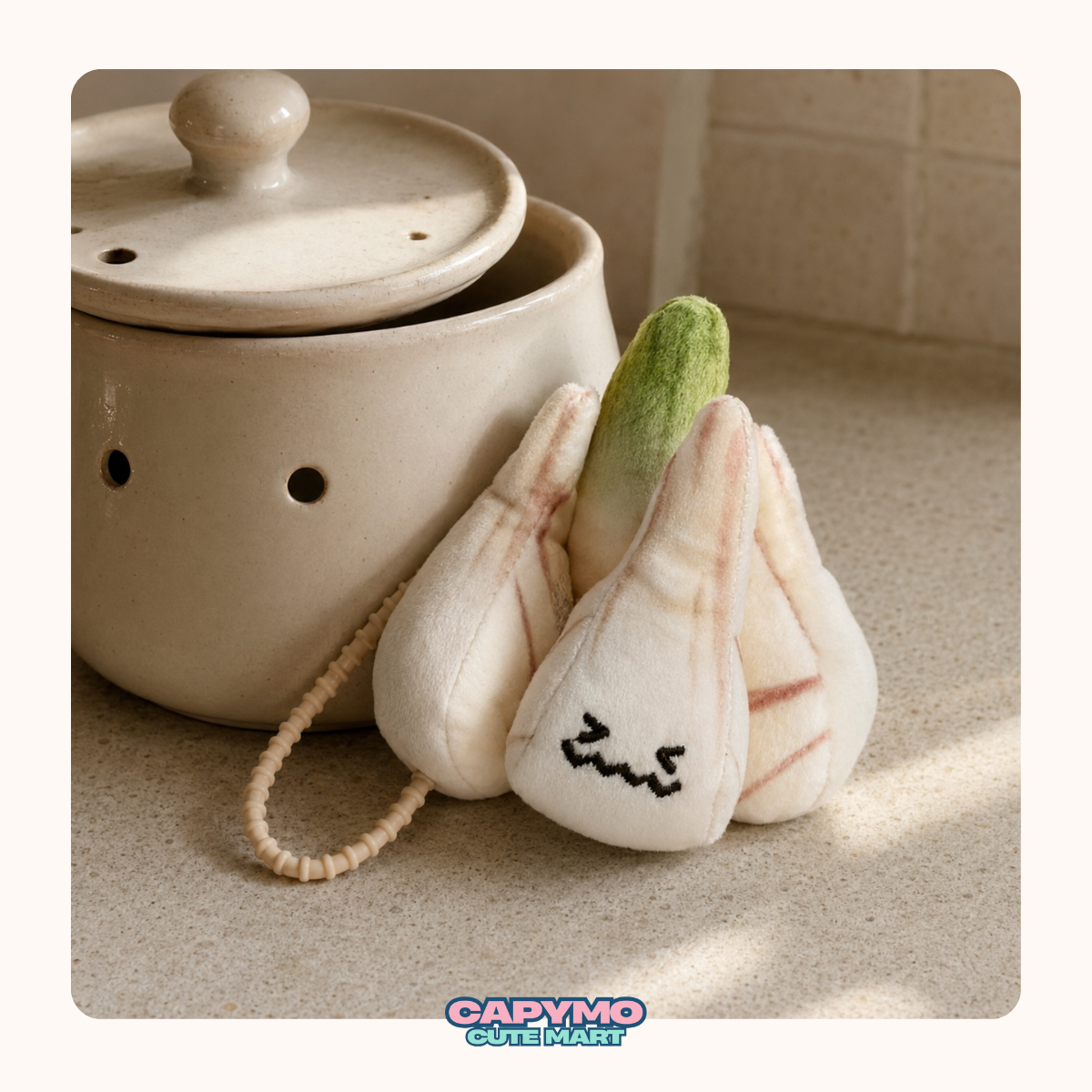 A cute plush garlic bulb accessory with embroidered facial features and a hanging loop, styled next to a ceramic pot on a countertop.
