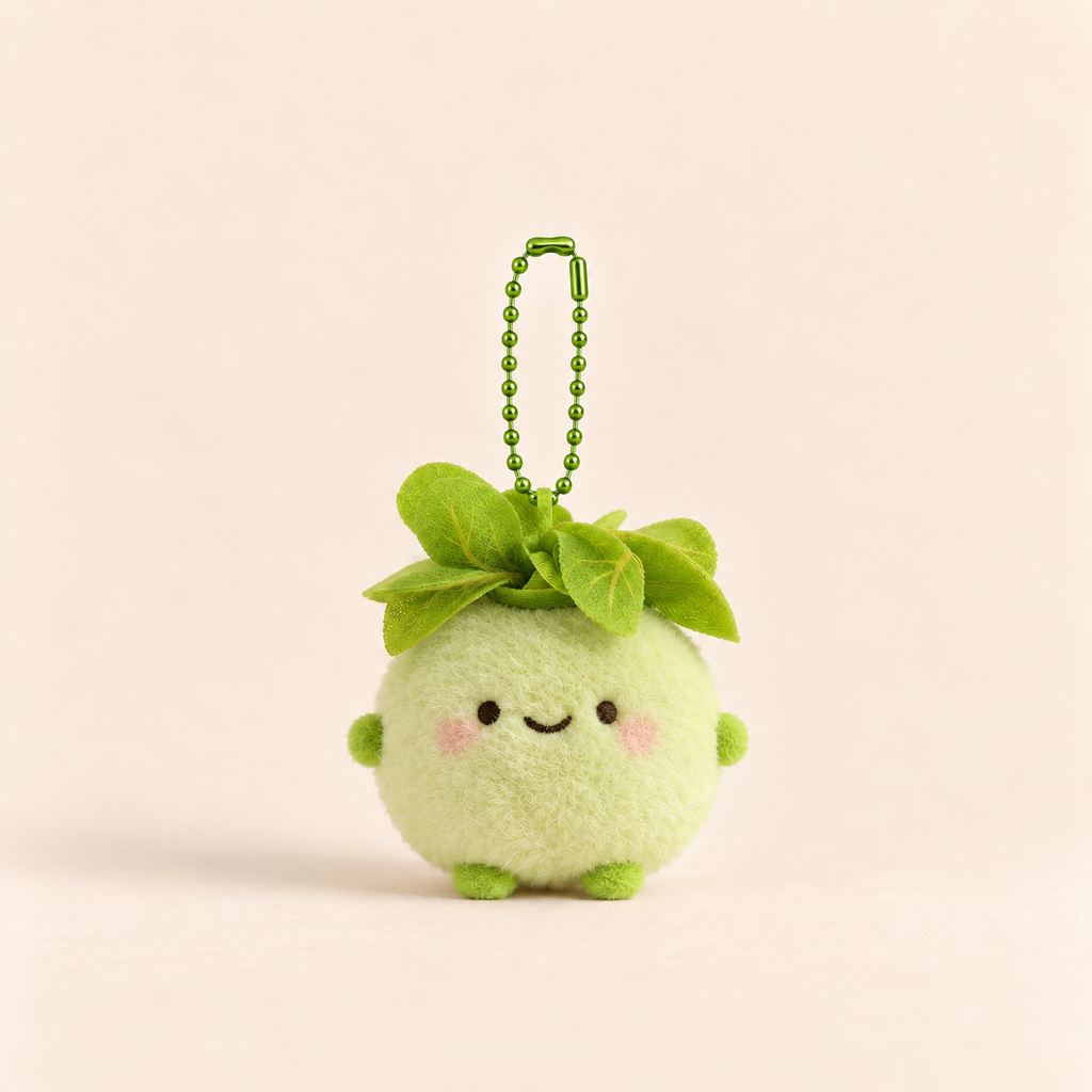 A cute, round green plush avocado keychain with embroidered facial features and a green ball chain, set against a solid pale peach background.