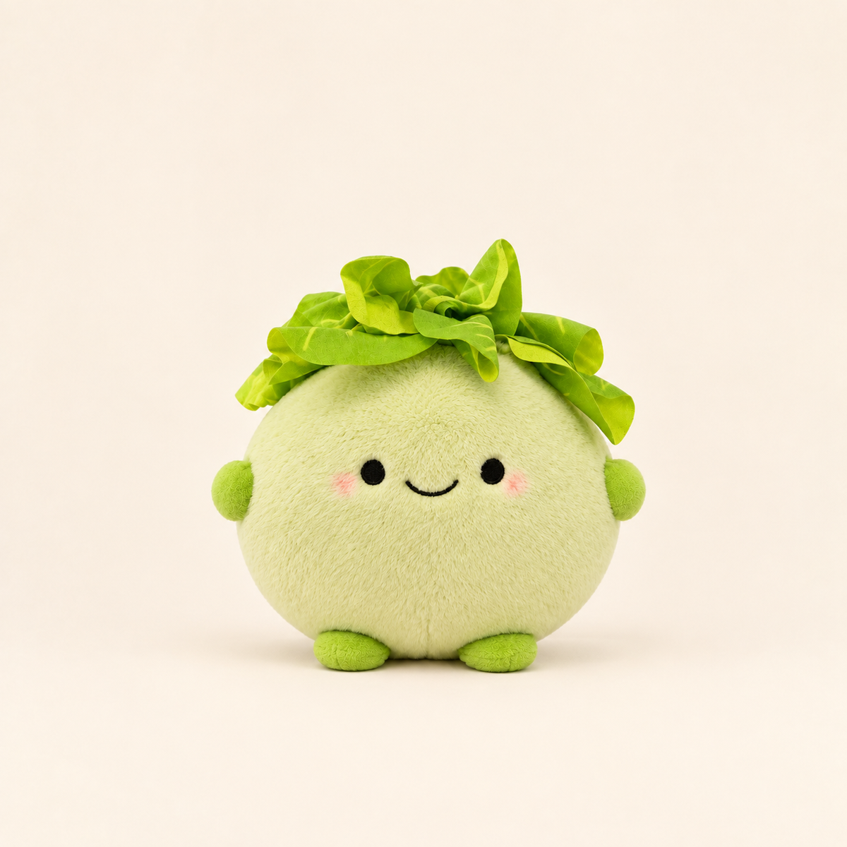 A cute, round plush toy shaped like a smiling green vegetable or character with leafy green hair, pink cheeks, and small green hands and feet, centered on a warm off-white background.