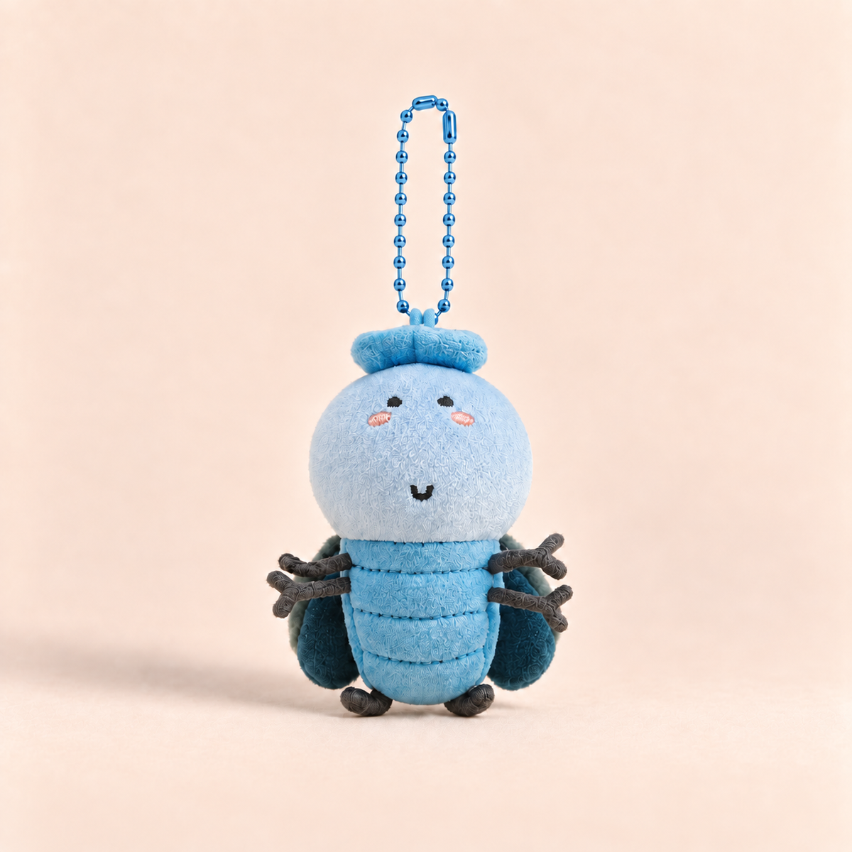 A cute blue felt insect plush keychain charm with a blue ball chain, set against a solid pale peach background.