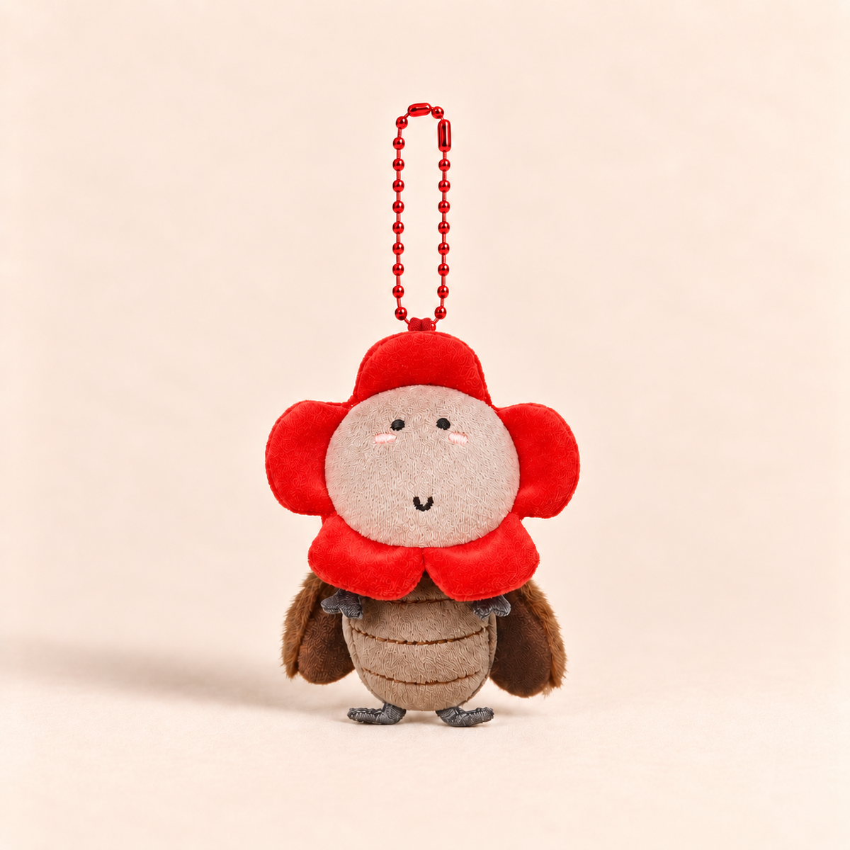 A small plush character keychain shaped like a flower-bird hybrid, featuring a red flower crown and collar, a beige face and belly, and brown wings, attached to a red ball chain against a warm beige background.