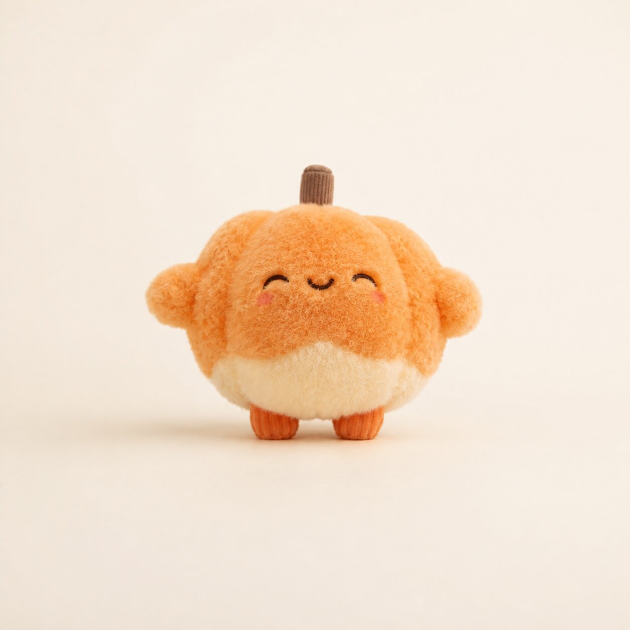 A cute, round plush toy shaped like a smiling orange pumpkin with a small brown stem on top, photographed against a clean, solid off-white background.