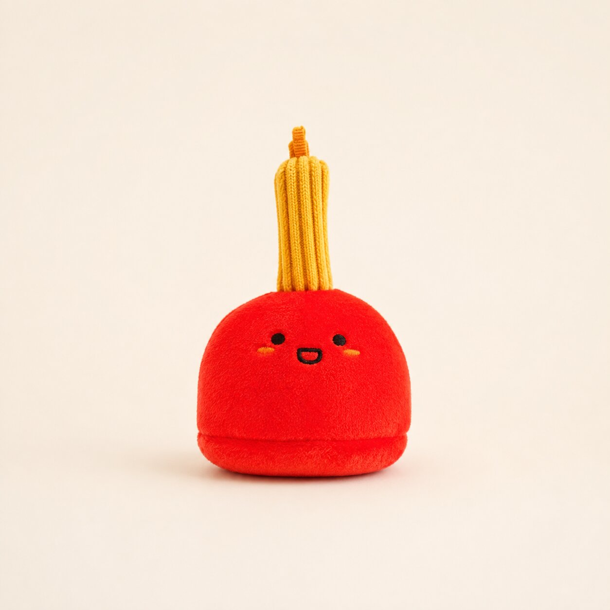 A cute red plush toy shaped like a small character with yellow cord-like hair, photographed against a plain warm off-white background.