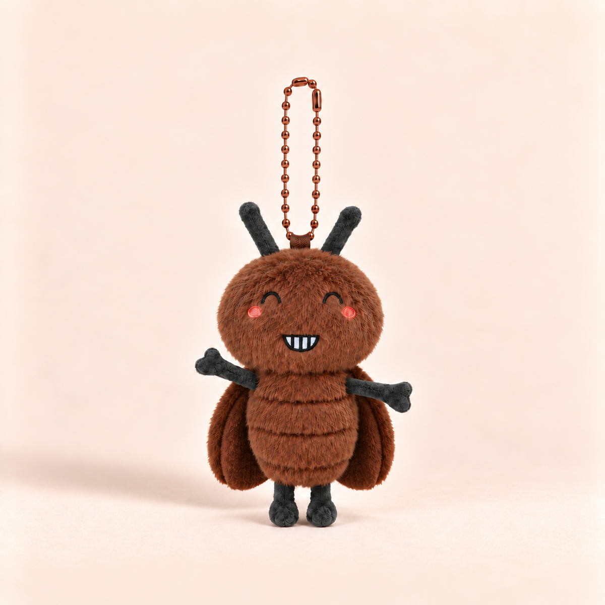 A brown plush bug-shaped keychain charm with black antennae, arms, and legs, pink embroidered cheeks, and a smiling toothy mouth, hanging from a brown bead chain against a soft beige background.