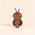 A cute, soft plush toy of a smiling cockroach, featuring a brown body, dark gray legs and antennae, and pink cheeks, set against a solid light beige background.