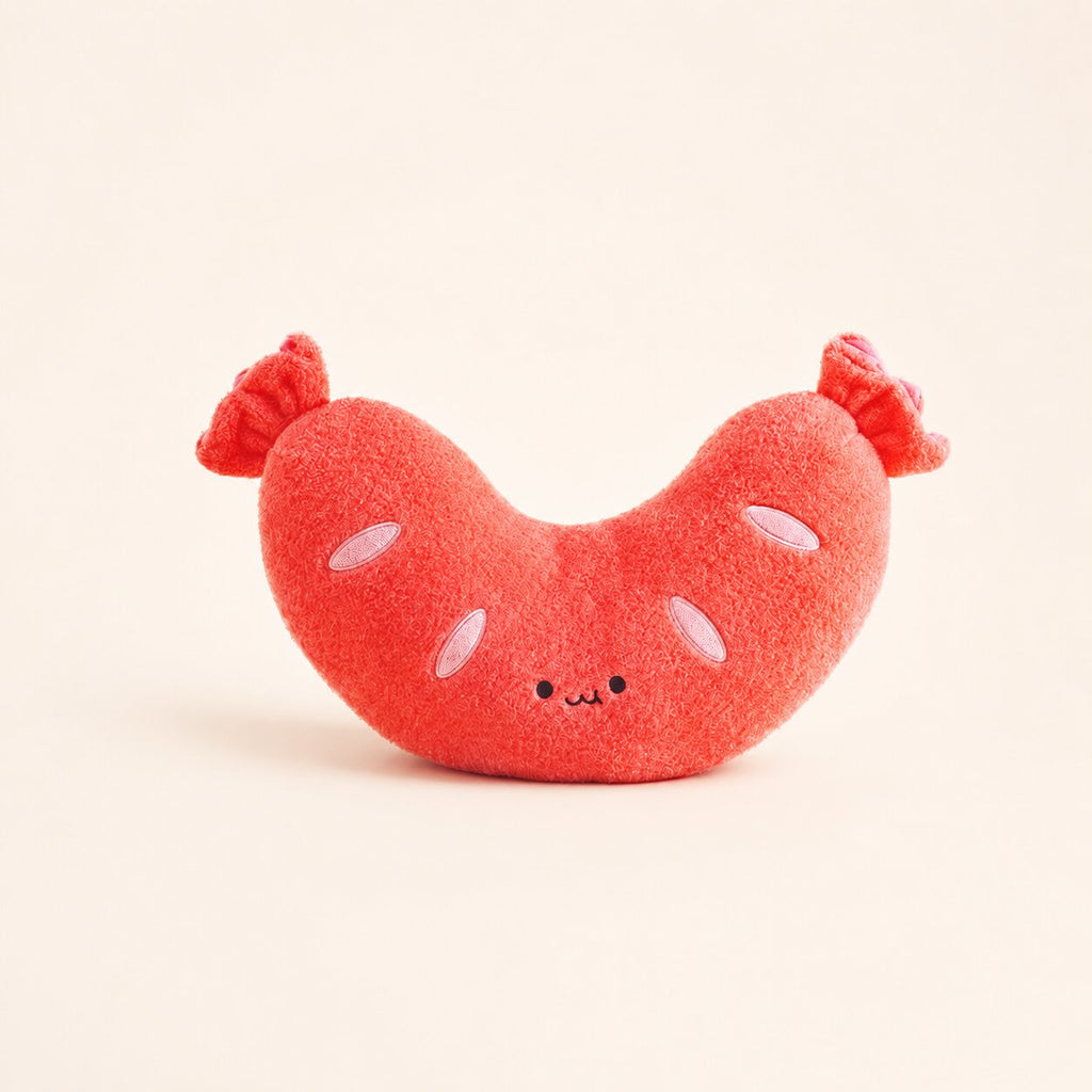 A cute, plush sausage-shaped toy in a vibrant coral red color, featuring embroidered facial features and pinkish-red tail tips, set against a solid cream background.