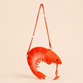 A bright red plush shrimp-shaped crossbody bag with a matching red shoulder strap, shown against a solid light beige background.