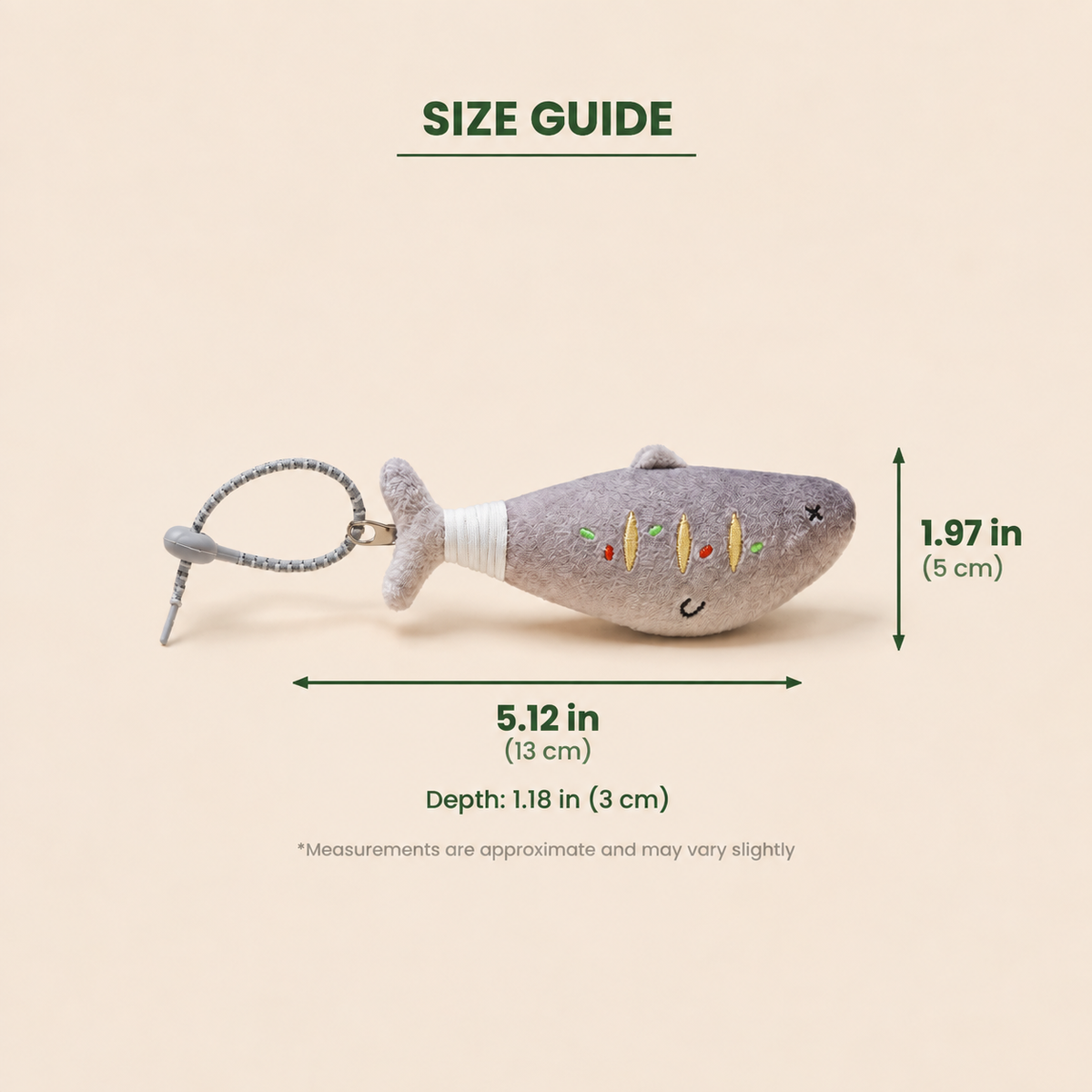 A gray plush fish keychain with a white wrapped neck and small embroidered facial details, shown on a beige background with overlaid size guide measurements labeled 5.12 in length, 1.