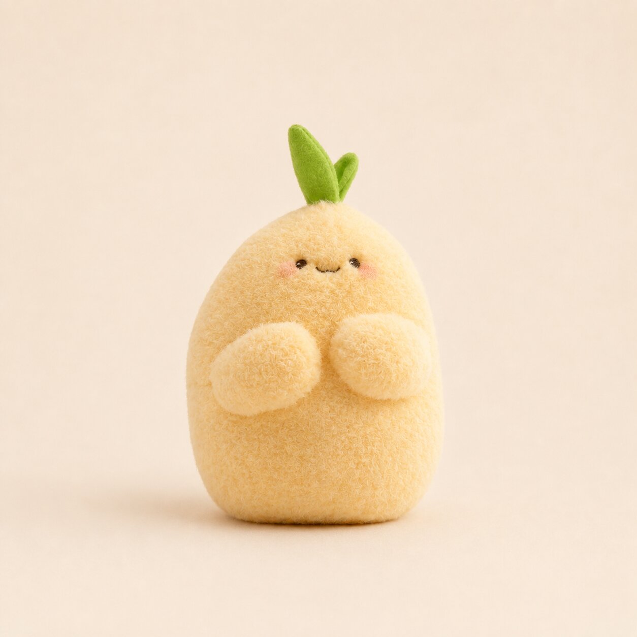 A cute, soft plush toy shaped like a round, smiling pale yellow fruit or dumpling with two small green leaves on top, photographed against a warm beige background.