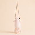 A plush octopus-shaped shoulder bag in pale pink and cream, featuring a long tan strap and a small embroidered face, set against a solid light beige background.
