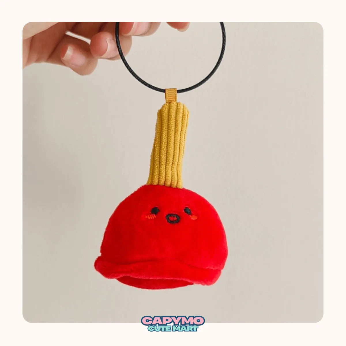 Red bell-shaped plush toy with a yellow handle, held by a hand against a plain background.