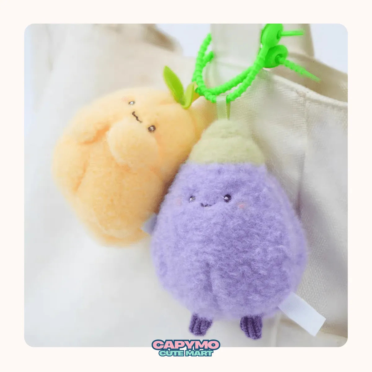 Two plush keychains, one orange and one purple, with a green clip on a white background. Brand 'Capymo' is visible.